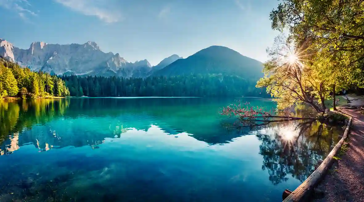 Lago al amanecer, rodeado de árboles verdes y montañas