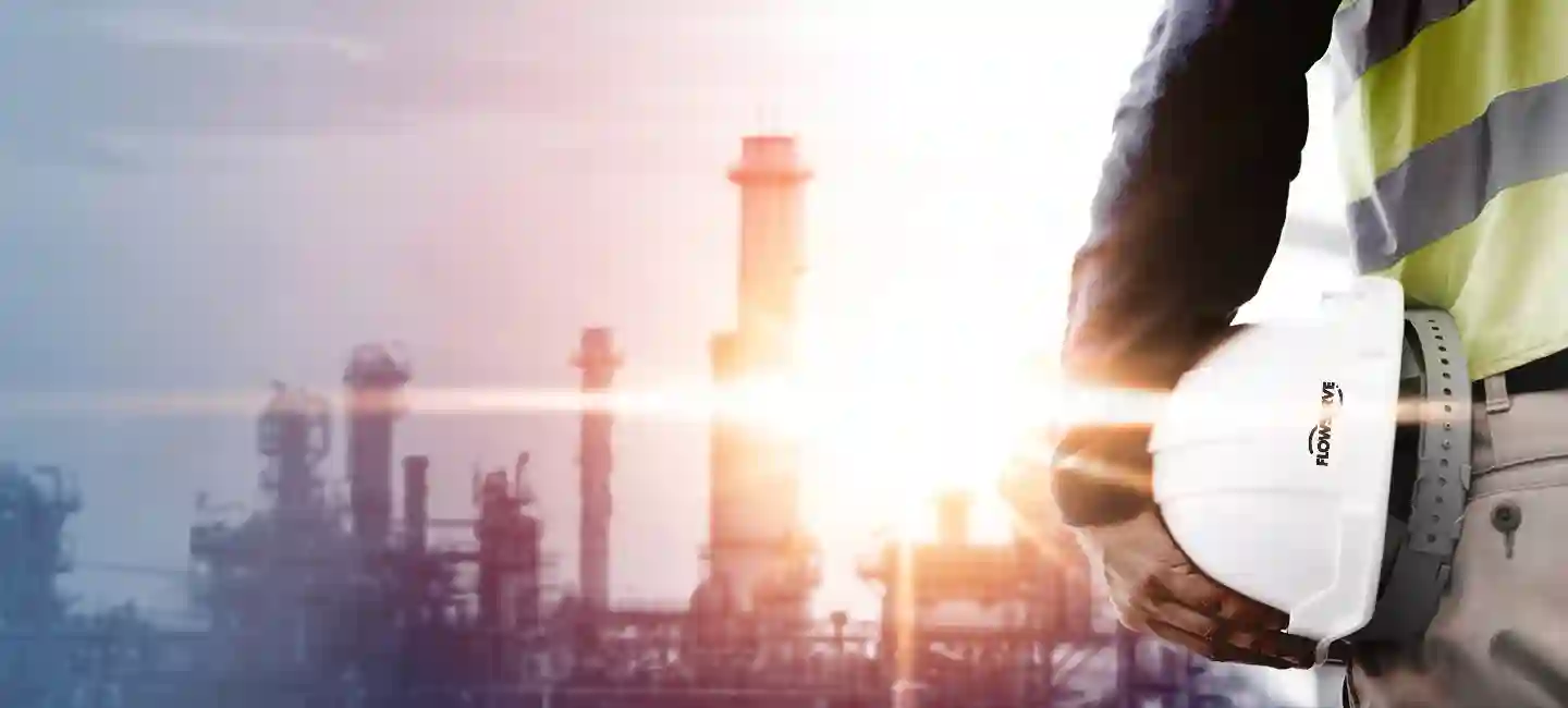 Man holding hard hat and facing a sunrise overlooking a manufacturing plant